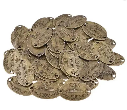 Ovalt metallmerke med teksten Handmade i slitt messingfarge